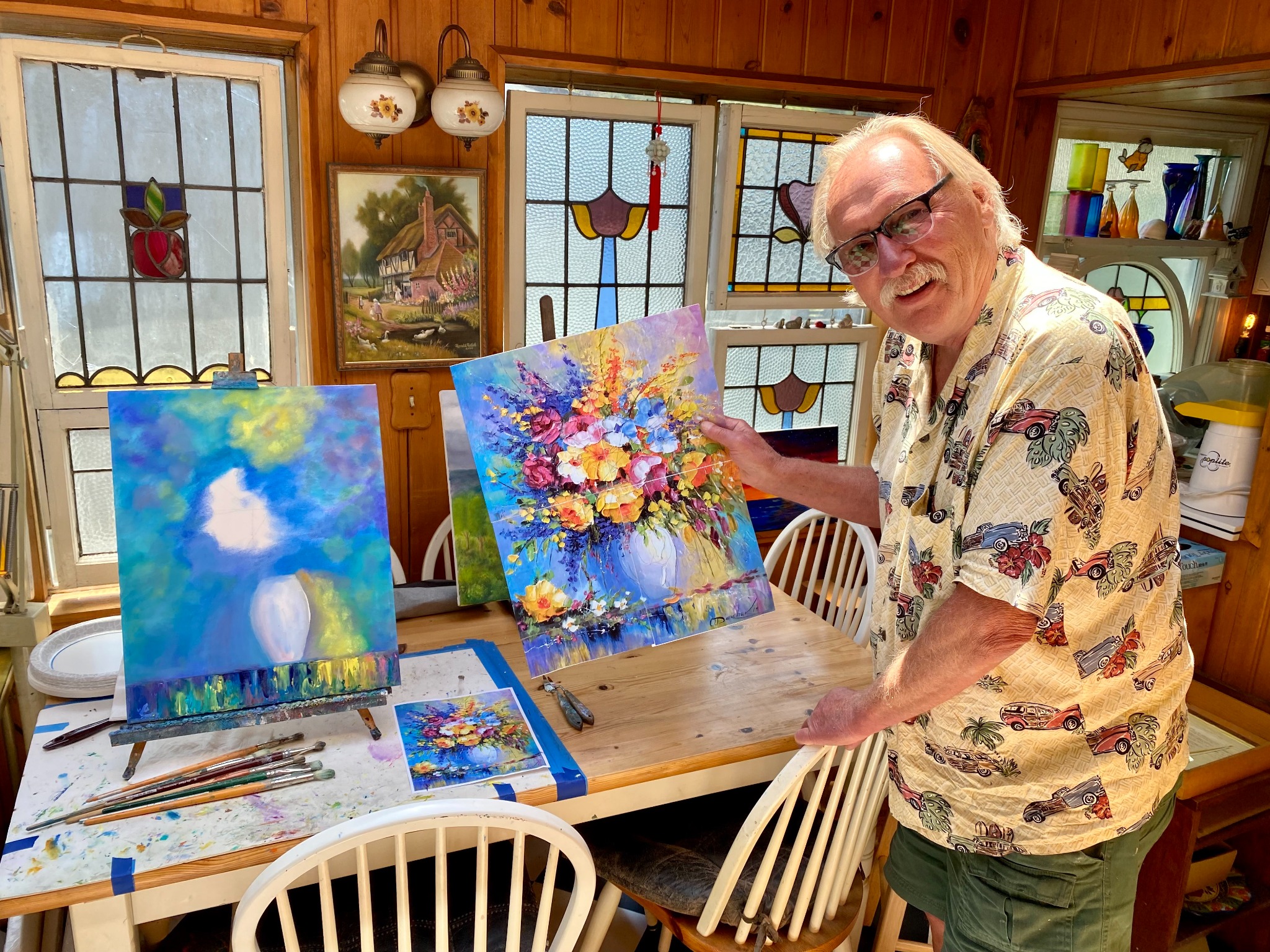 Larry Wall in his home art studio holding a colorful floral painting